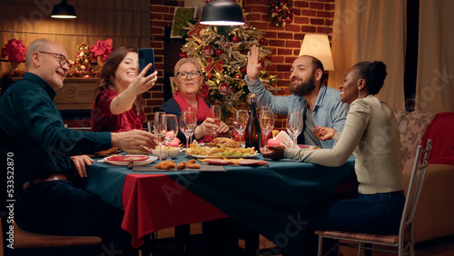 Beautiful woman presenting Christmas dinner to friend through smartphone internet video call. Festive family on cellphone online call with relatives wishing them Happy Holidays.
