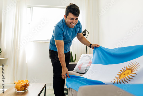 Young Argentinian man preparing home to watch soccer game with friends