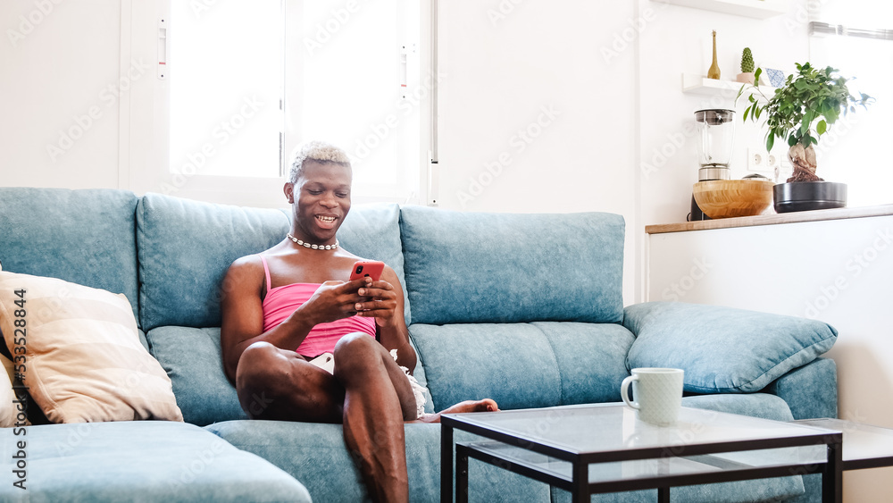 African Black transsexual man in stylish feminine clothes texting on cellphone on couch African Black transsexual man in stylish feminine clothes texting on cellphone on couch