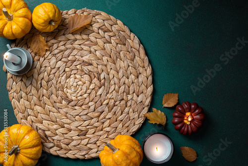 Cozy hygge table. Top view of wicker place mat  pumpkins  autumn leaves  candle on dark table. Autumn table setting. Festive Thanksgiving background. Restaurant menu. Copy space