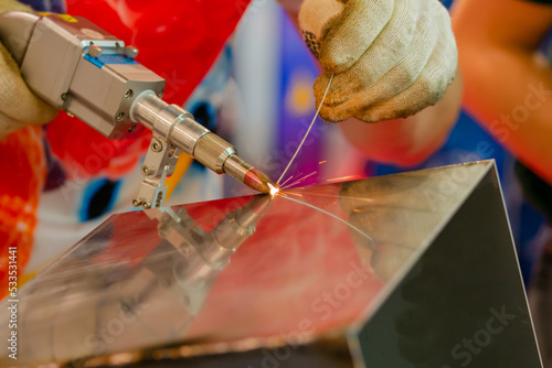 Welder hands using portable handheld laser welding machine with sparks - close up. Manufacturing, industrial, equipment, technology and metalworking concept
