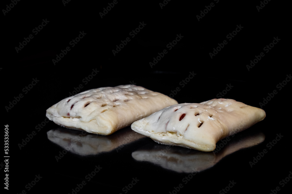 Two uncooked puff pastry buns with red strawberry jam on tray in electric oven, black background. Homemade bakery, food, cooking, pastry, semi-finished products and raw concept