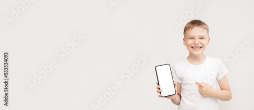 Smiling fair-haired boy in white t-shirt points his finger at the smartphone screen. banner