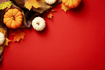 Autumn plaid with maple leaves and pumpkins on red background. Hygge, cozy style flatlay composition.