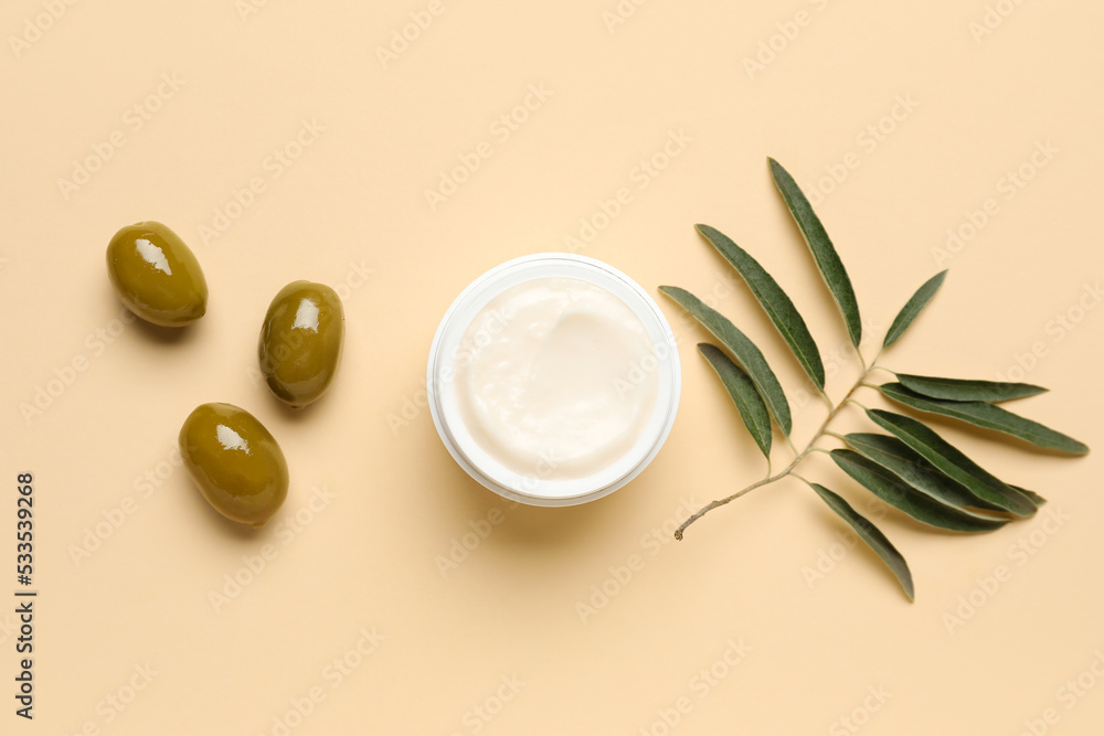 Jar of cream with green olives and plant branch on beige background Jar of cream with green olives and plant branch on beige background