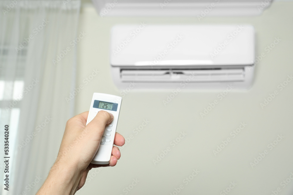 Man operating air conditioner with remote control indoors, closeup Man operating air conditioner with remote control indoors, closeup