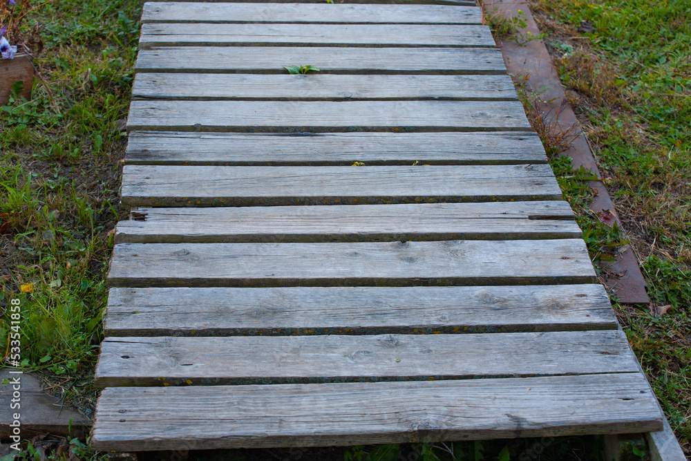 The path of unpainted boards lies on the green grass The path of unpainted boards lies on the green grass