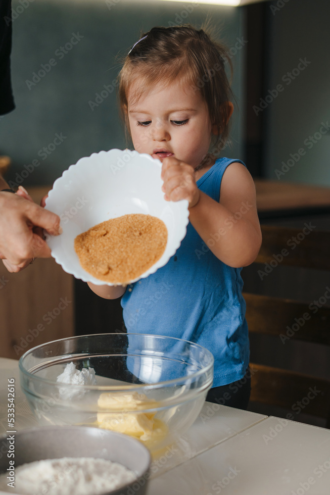 The mother helping her daughter turn the bowl of cocoa over the dough prepared for baking. For lifestyle design. People lifestyle. The mother helping her daughter turn the bowl of cocoa over the dough prepared for baking. For lifestyle design. People lifestyle.