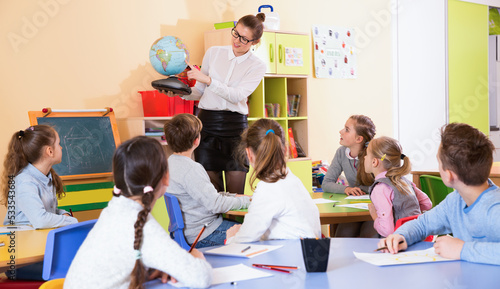 Tablou canvas Cheerful positive female teacher giving geography lesson in classroom, showing p