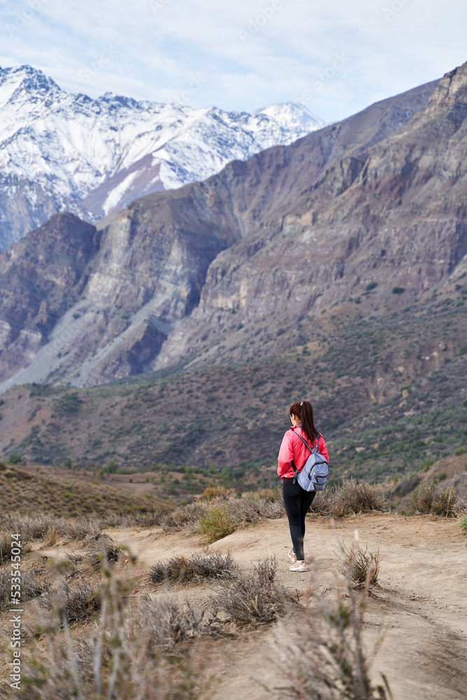 young woman with red jacket and backpack, descending the mountain in the middle of the Andes Mountains of Chile
