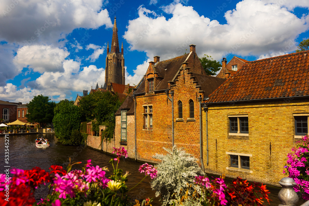 Peaceful photo of canal of Bruges with view of belfry under deep blue cloudy sky.