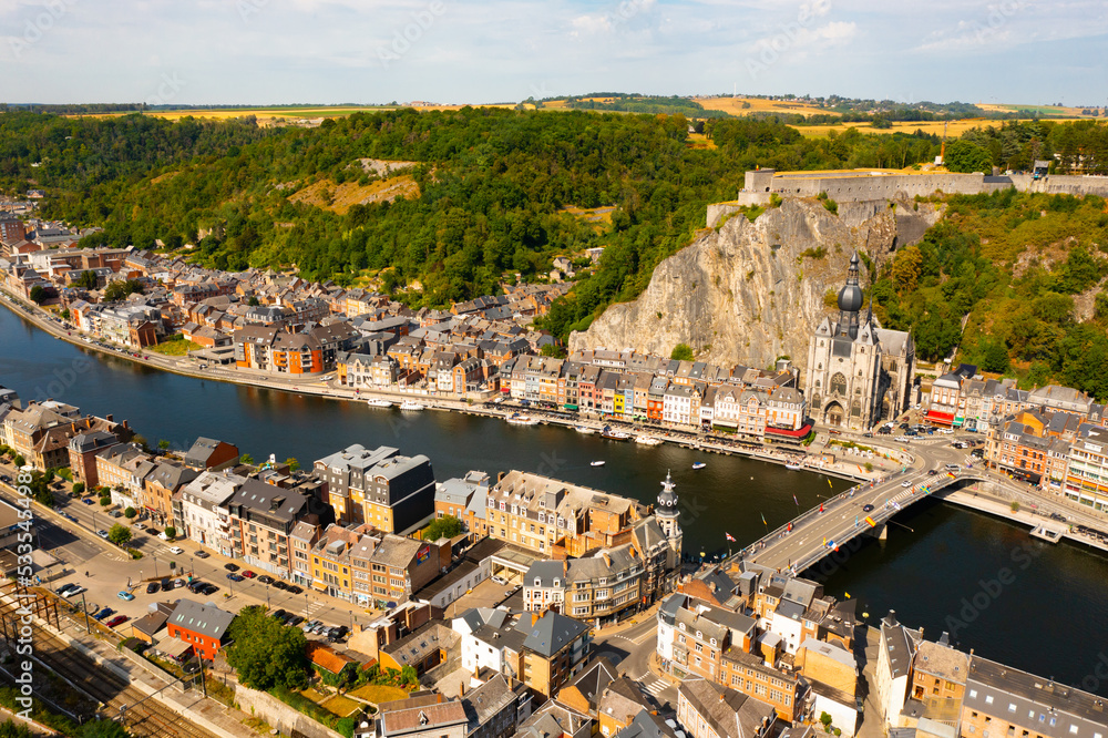 Scenic summer view of Dinant cityscape on banks of river Meuse overlooking Collegiate Church of Notre Dame and fortified Citadel on top of cliff overgrown with green trees, Namur province, Belgium