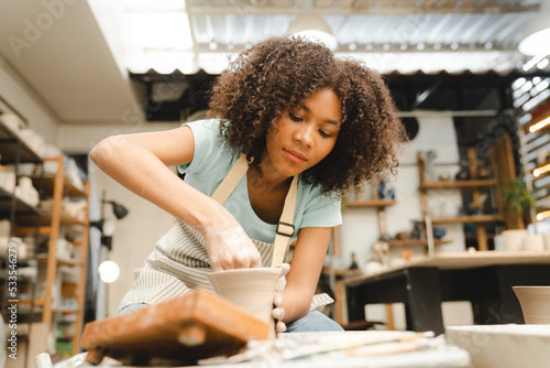 Bilde på lerret Creative afro American young woman artist molding clay on pottery wheel, Worksho