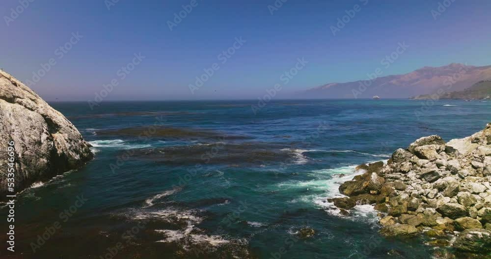 Flying low above the blue water of the Pacific Ocean. Algae floating on the water surface. Mountains of California at hazy backdrop. Flying low above the blue water of the Pacific Ocean. Algae floating on the water surface. Mountains of California at hazy backdrop.
