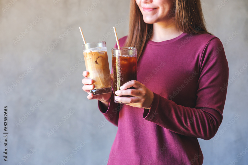 Closeup image of a young woman holding and drinking two glasses of iced coffee Closeup image of a young woman holding and drinking two glasses of iced coffee