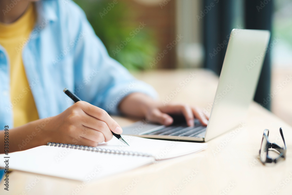 Close up of woman studying, reading book, and taking notes using laptop. Close up of woman studying, reading book, and taking notes using laptop.