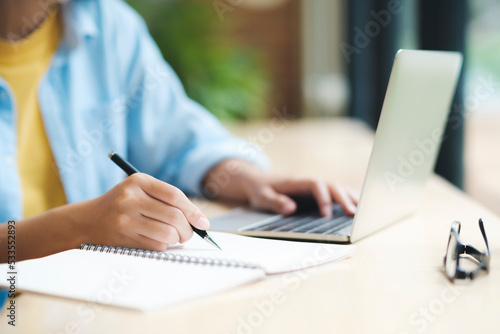 Close up of woman studying, reading book, and taking notes using laptop.