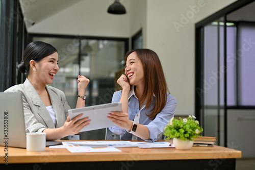 Two happy and surprised millennial Asian businesswomen celebrate their success together