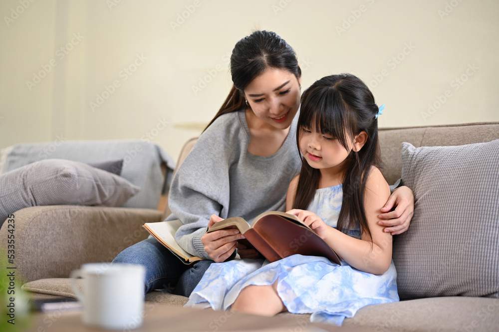 Lovely and relaxed Asian mom reading a book or telling fairy tale story to her cute daughter Lovely and relaxed Asian mom reading a book or telling fairy tale story to her cute daughter