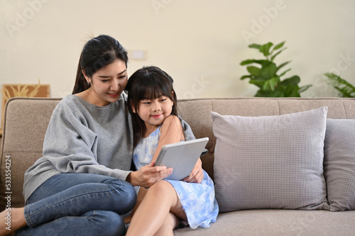 A pleased Asian mom using tablet, reading an online fairy tale story to her daughter