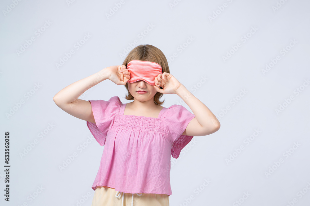 Young tired woman with sleeping mask yawning on white background