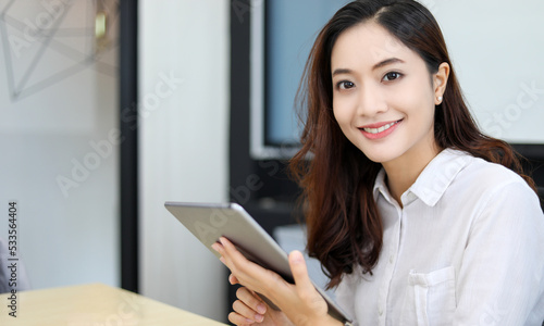 Smiling Asian businesswoman using tablet for work and doing internet research in her office.