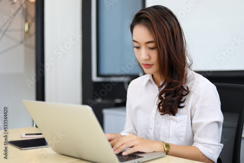 Asian businesswoman using laptop for work and doing internet research in her office.