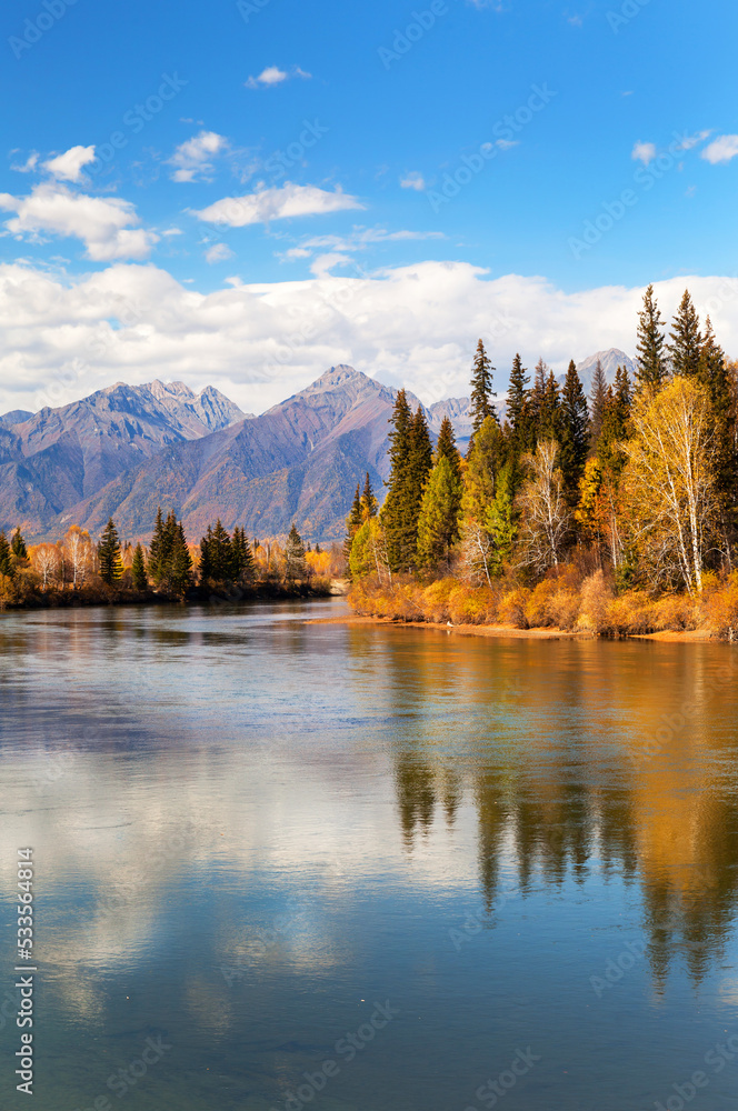 Autumn in highlands. View from river bank to mountain range and yellowed forest on bank of calm river. Baikal region, Buryatia, Eastern Sayan Mountains, Irkut River, Tunka valley, Nugan village