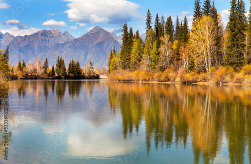 Picturesque autumn landscape with reflection of mountains and yellowed forest in calm blue water. Buryatia, Tunka foothill valley, Nugan village