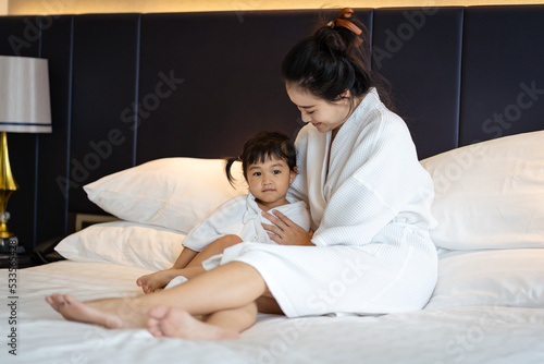 Asian little girl and her young mother in a bathrobe having fun and using a good time on the bed. Selective focus.