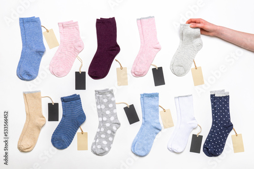 Female hand holding socks among women's cotton socks set with price tags on white background. Fashionable socks store. Socks shopping, sale, merchandise, advertisement concept