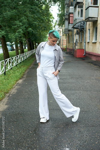 A woman with green hair in white clothes and with an umbrella walks down the street after the rain