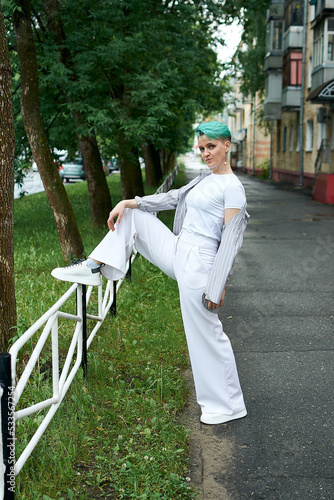 A woman with green hair in white clothes and with an umbrella walks down the street after the rain
