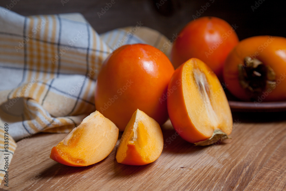 Whole ripe persimmon and sliced fruit on a wooden background..