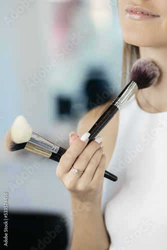 The girl is holding make-up tools. Professional make-up artist with a belt bag with tassels. makeup brushes. Professional Make-up artist doing glamour model makeup at work.