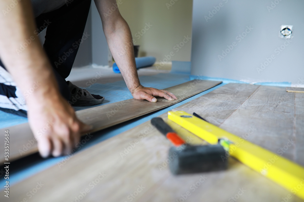 Installing laminated floor, detail on man hands blue wooden tile, over white foam base layer, small pile with more tiles background Installing laminated floor, detail on man hands blue wooden tile, over white foam base layer, small pile with more tiles background