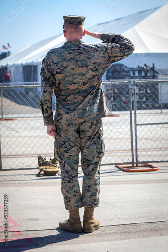 A military man saluting wearing camouflage photographed from behind