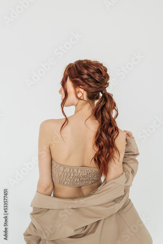 beautiful young red-haired woman with a hairstyle, curly hair stands with her back on a white background. concept of hair care, barbershop and hair stylist