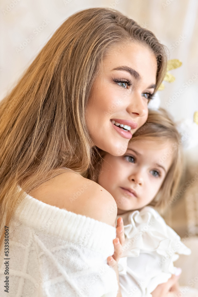 Mom and daughter hug each other, sitting on the bed in a bright bedroom.Family. Ethno-interior design Mom and daughter hug each other, sitting on the bed in a bright bedroom.Family. Ethno-interior design