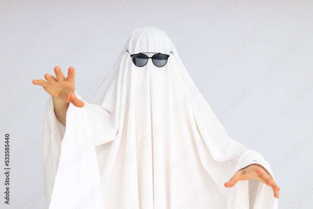 Concept of Halloween, woman in ghost costume and sunglasses on light background