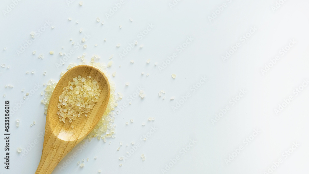 Flavored yellow bath salt in wooden spoon on white background top view Flavored yellow bath salt in wooden spoon on white background top view