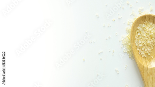 Flavored yellow bath salt in wooden spoon on white background top view