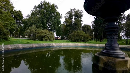 Drone forward moving shot over an old fountain in a park covered with lush green vegetation at daytime. photo