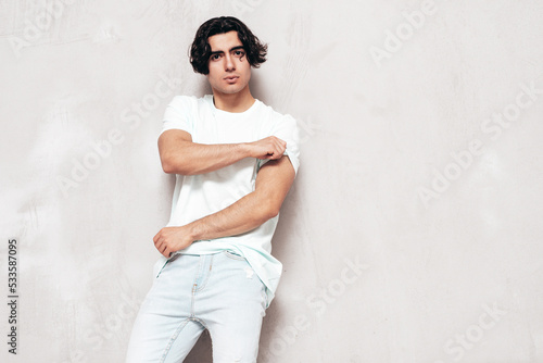 Portrait of handsome confident  stylish hipster lambersexual model.Sexy man dressed in over size T-shirt and jeans. Fashion male isolated in studio. Posing near grey wall © halayalex