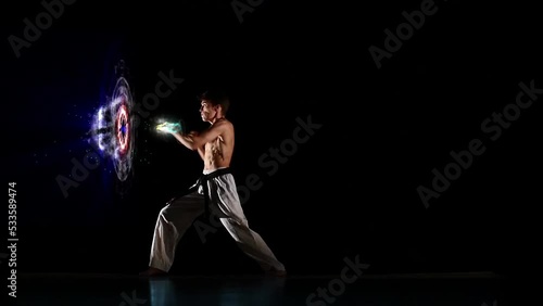 Male kyokushinkai karate performing kata on black studio background. Athlete delivers punches fists. Blows with the effect of 3D rendering of computer graphics in the form of blue holographic circles. photo