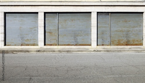 Shop retail with rusty metal shutters closed . Concrete sidewalk and asphalt road in front. Urban background for copy space.