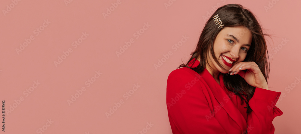 Happy young caucasian woman with snow-white smile looks at camera on pink background. Brunette woman with loose hair is wearing red jacket. Lifestyle, different emotions, leisure concept. Happy young caucasian woman with snow-white smile looks at camera on pink background. Brunette woman with loose hair is wearing red jacket. Lifestyle, different emotions, leisure concept.