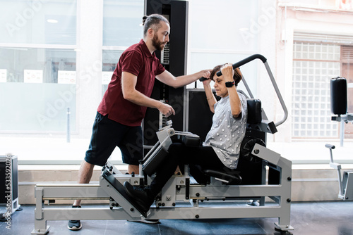 Older woman working out on the machines at the gym with her personal trainer