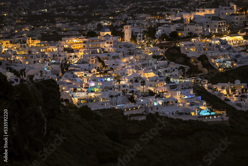  Illuminated whitewashed houses with terraces and pools and a beautiful view in Oia on Santorini island, Greece © wjarek