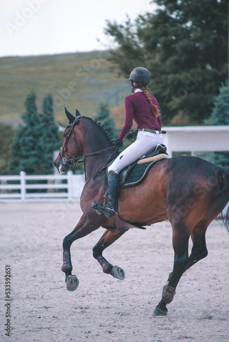 Young girl on sorrel horse galloping on show jumping competition. Equestrian sport. Back view.